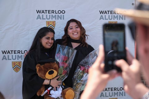 Two grads smiling for photos holding flowers and teddy bears. 