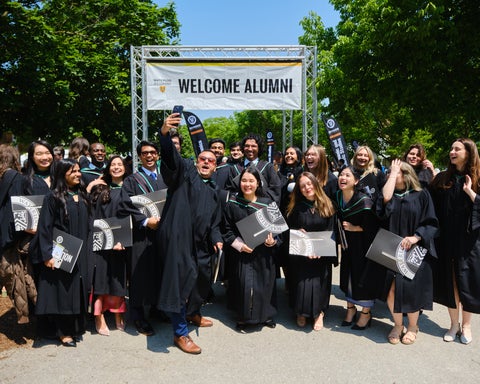 Group of graduates posing under Welcome Alumni banner