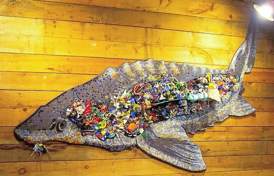 An 8-ft long glass tile mosaic sturgeon is filled with various examples of plastic waste affixed onto cardboard scales