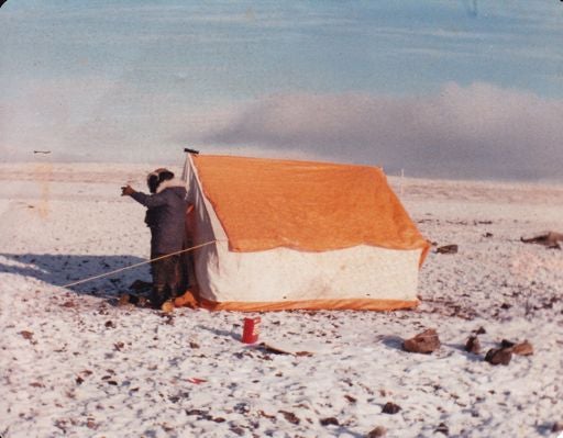 Resident standing beside a tent on snowy tundra.