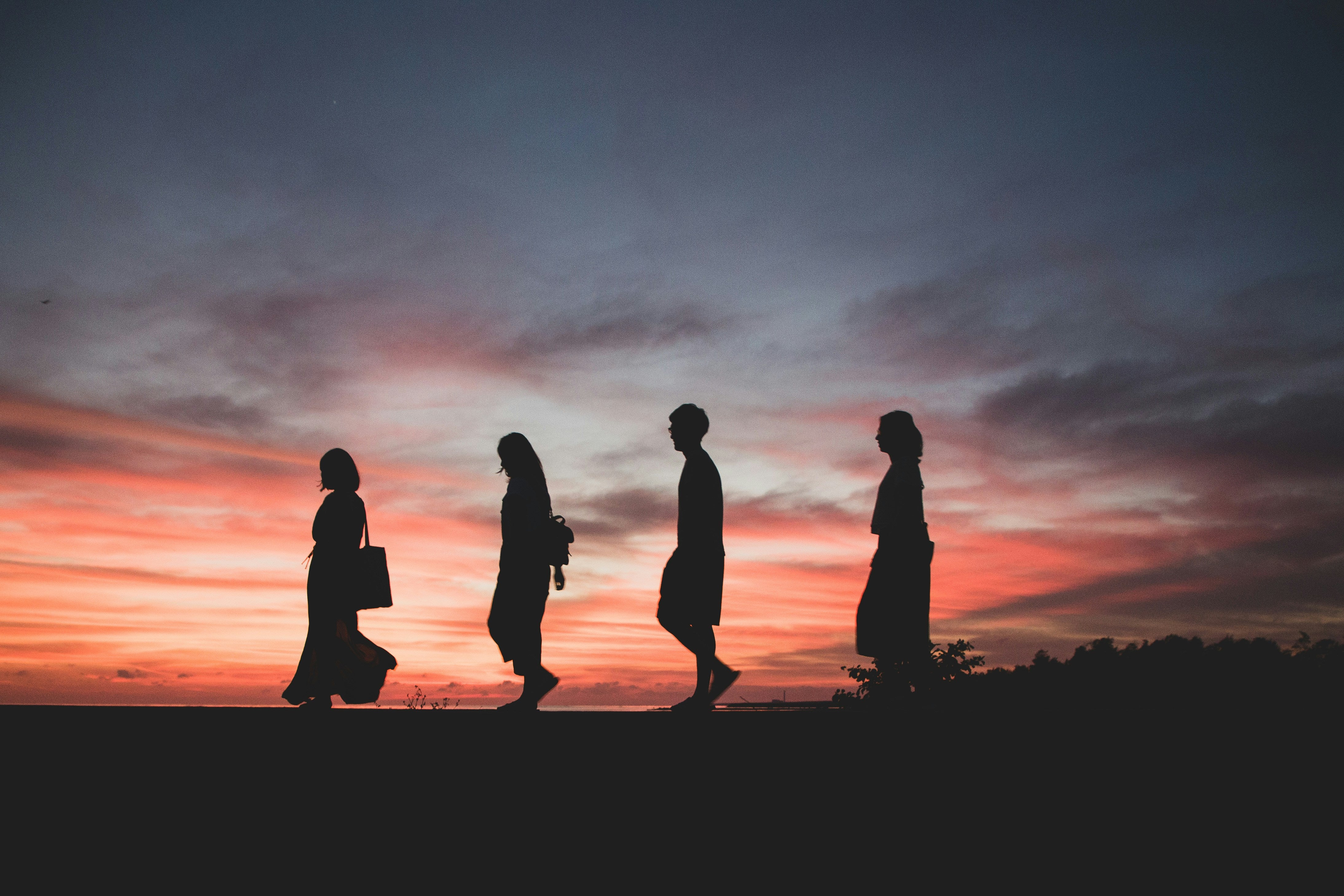 four silhouettes of people walking to the left, illuminated by a sunset in the background