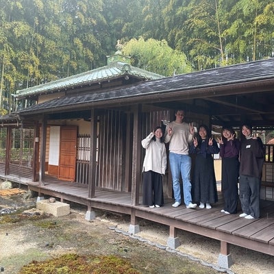Students stand on the porch of a rustic Japanese home.