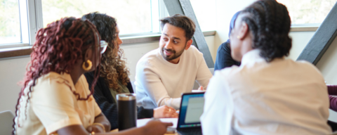 Group of students sitting at a table with laptops and talking