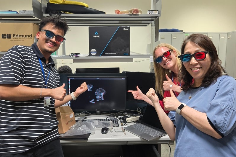 Three people standing wearing glasses with blue and red lenses smiling in front of a computer