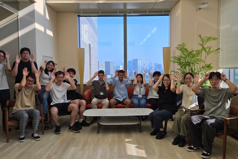 A group of people in an office setting posing for a photo and holding up their hands to their heads like animal ears.