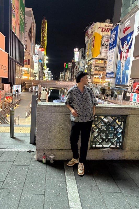 Rishabh Bajaj standing on a bridge over a river surrounded by tall buildings with advertisements on them.