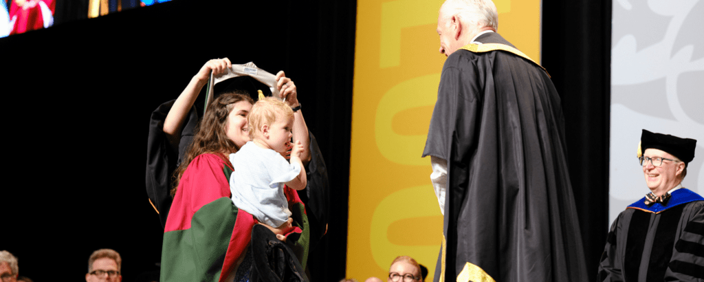 PhD graduate crossing the stage at convocation with child