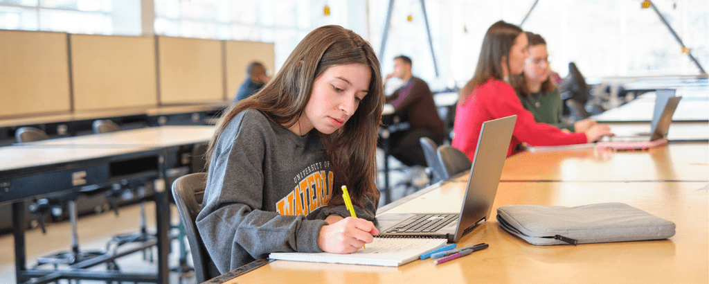 Student working on a laptop with a notebook