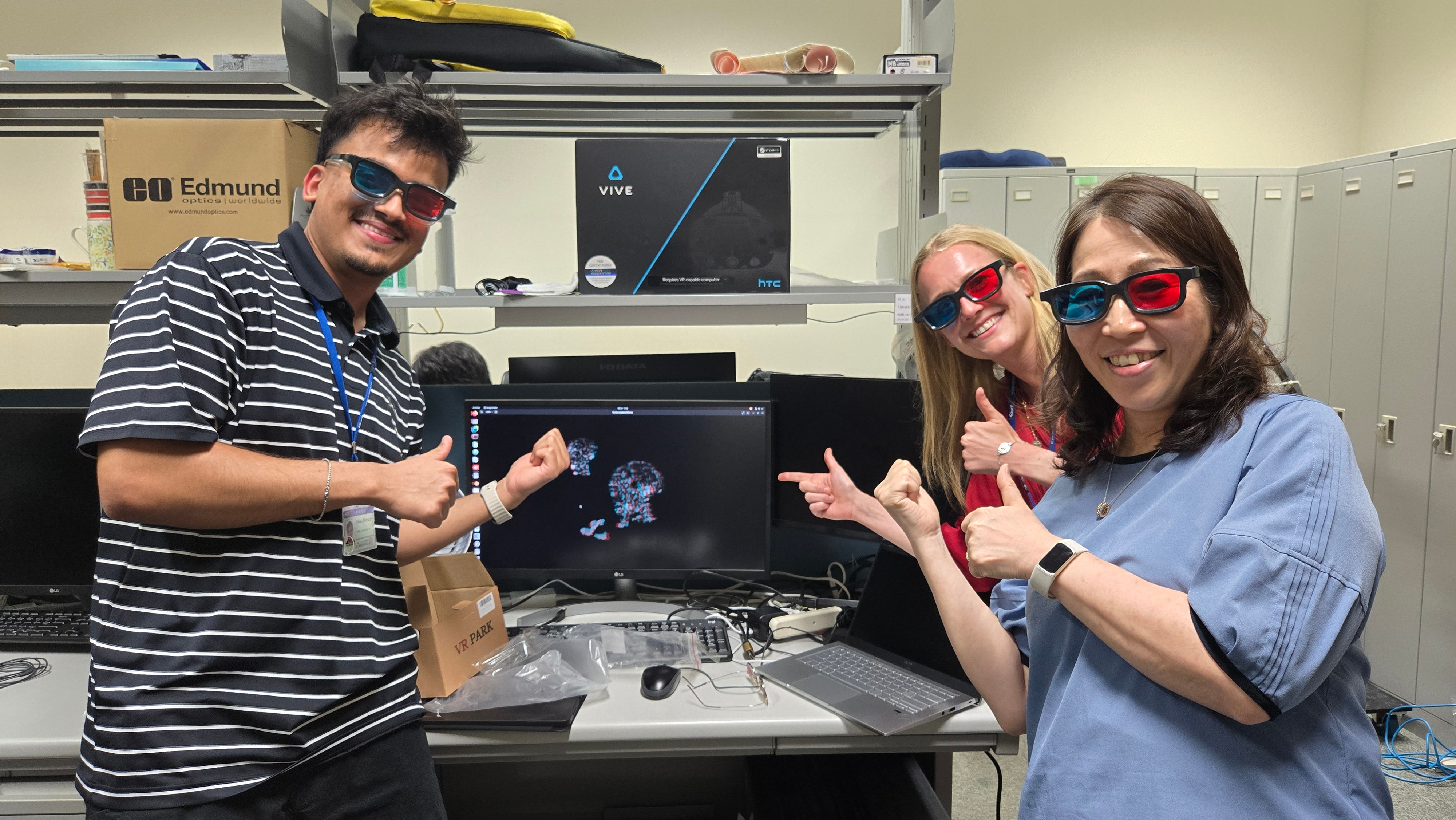Three people standing wearing glasses with blue and red lenses smiling in front of a computer