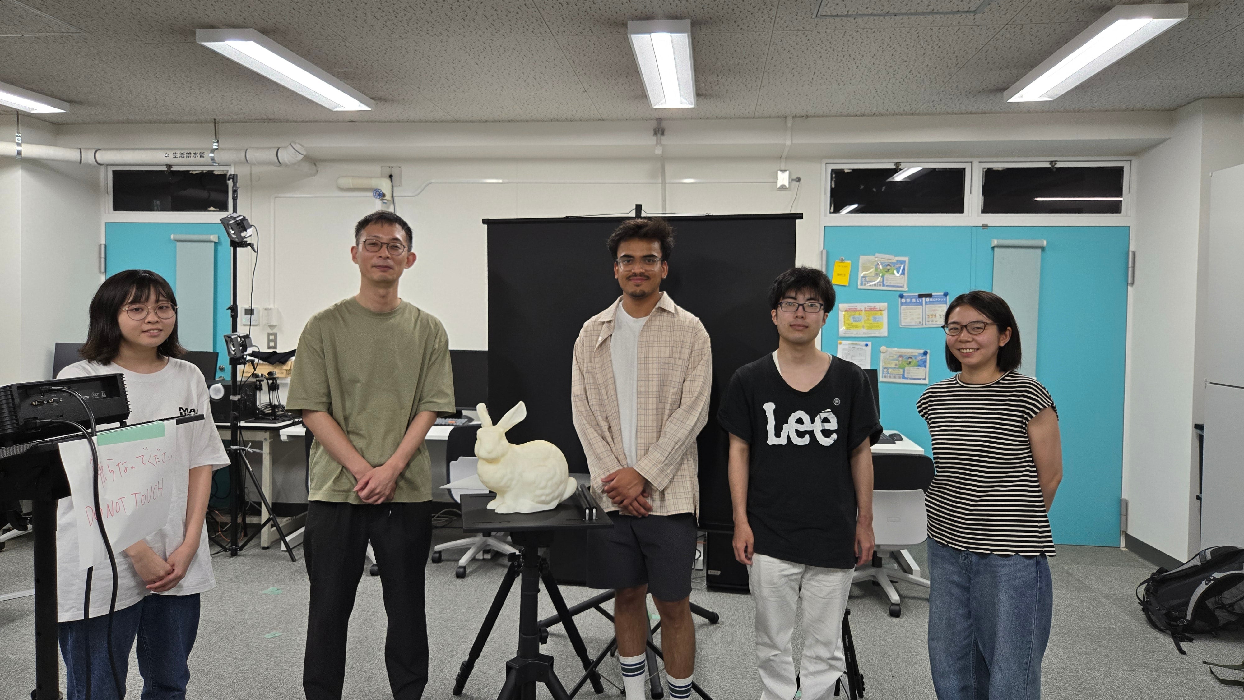 5 people standing in a line behind a ceremic rabbit in a classroom