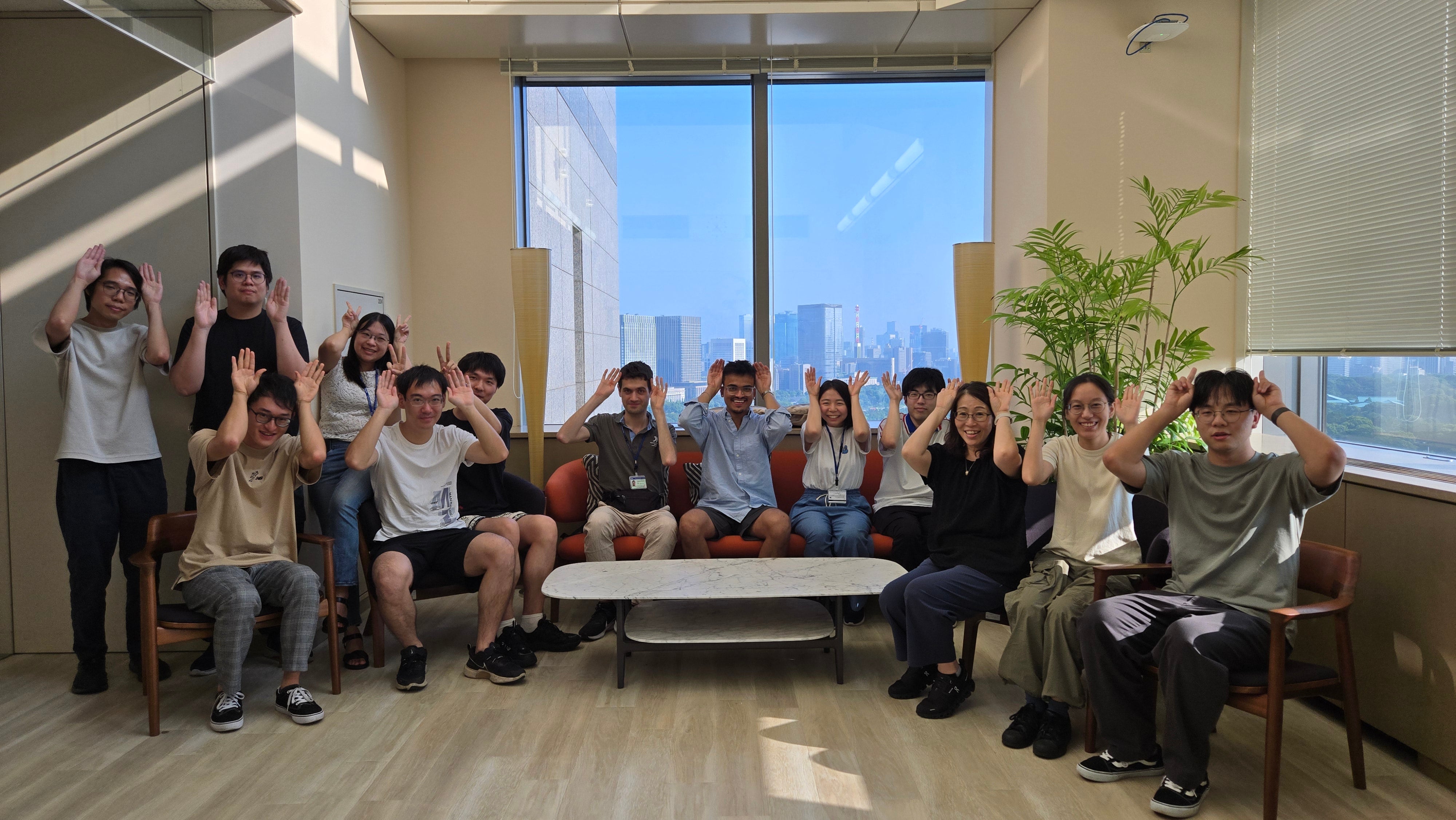 A group of people in an office setting posing for a photo and holding up their hands to their heads like animal ears.