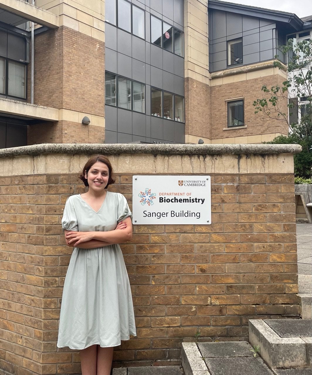 Atiyeh Ahmadi standing in front of a sign reading, "University of Cambridge: Department of Biochemistry - Sanger Building