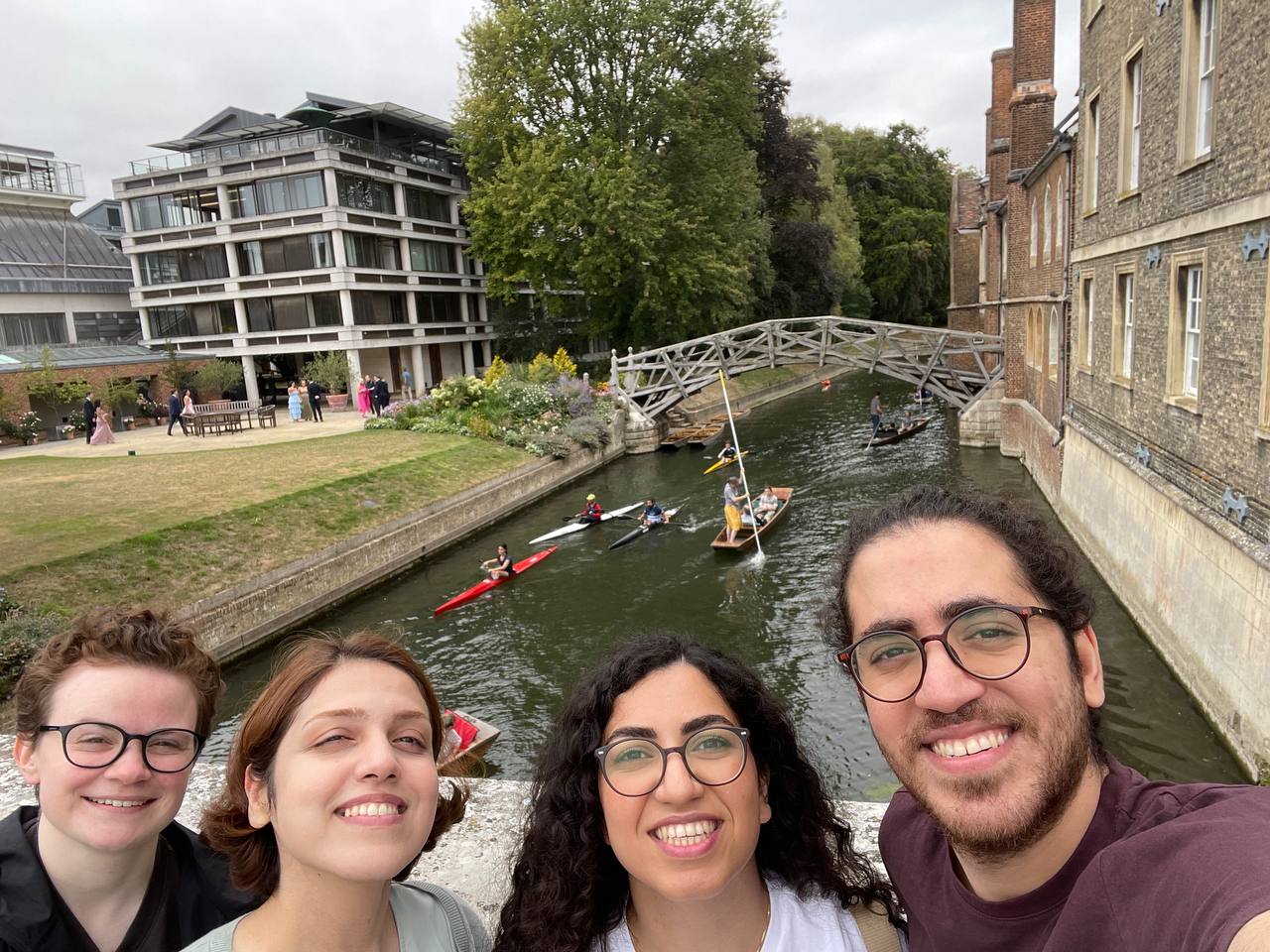 Four people take a selfie in front of a river where people are kayaking and canoeing.