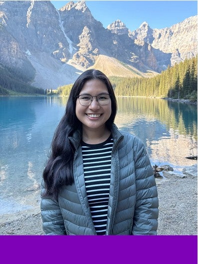 Graduate student Andrea Chakma with mountains and a lake in the background. A purple rectangle borders the bottom of the photo. 