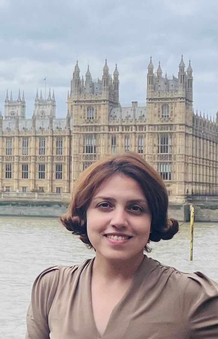 Graduate student Atiyeh Ahmadi standing across a river from a British government building
