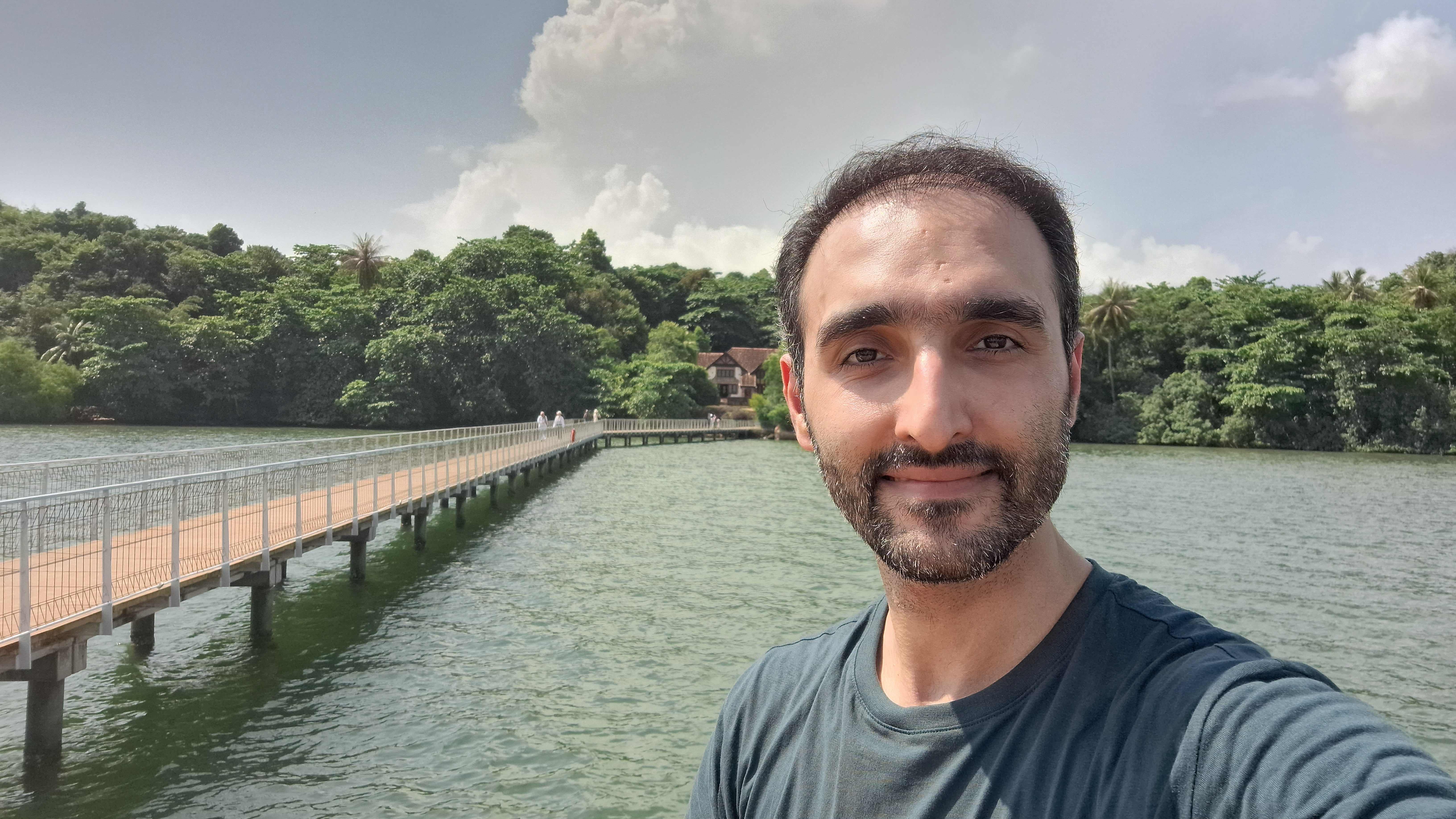 A selfie of Mohammad Shojaati with a bridge, a body of water, and a jungle in the background.