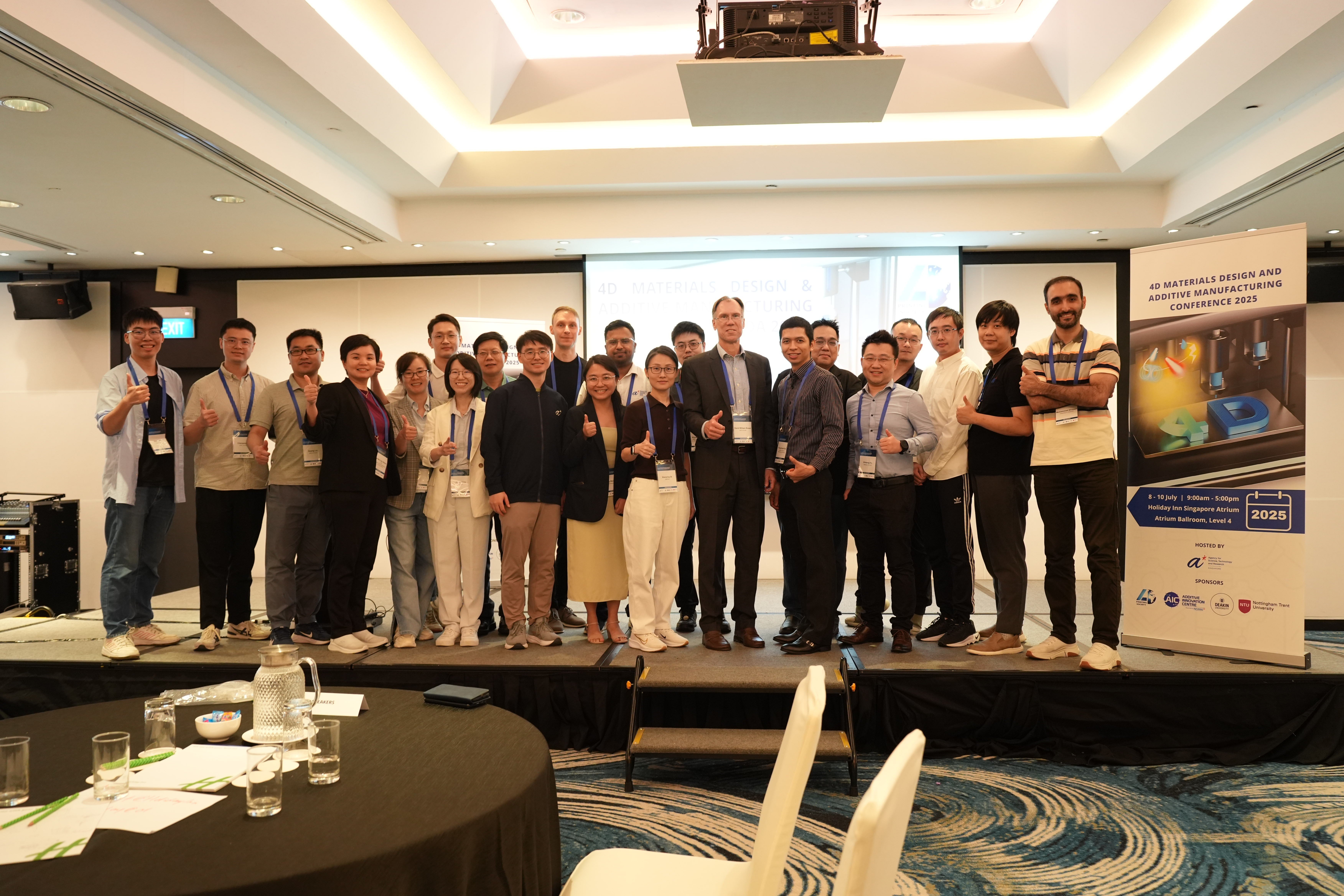 A large group of people standing up on a stage smiling and holding out thumbs ups