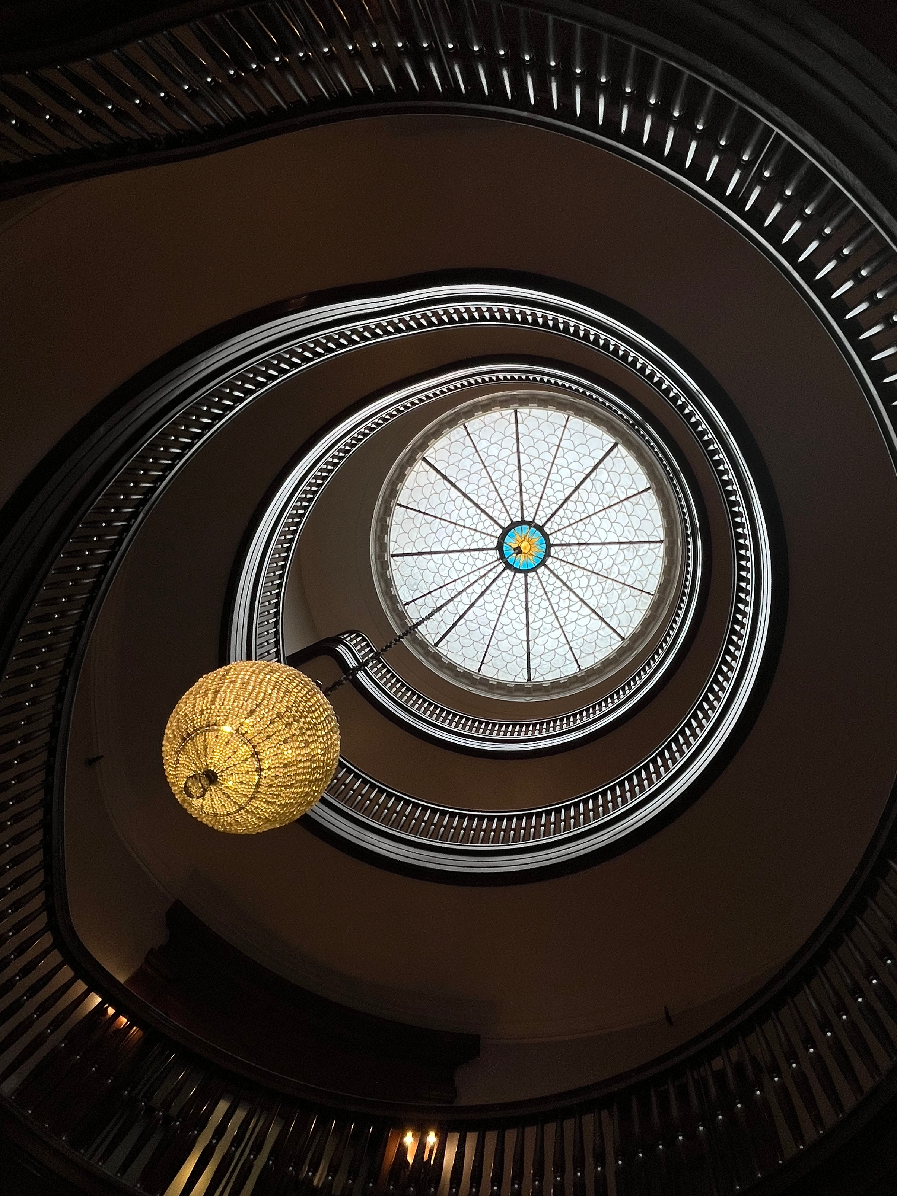 A photo looking up into a spiral staricase with a glass celing and a chandelier.