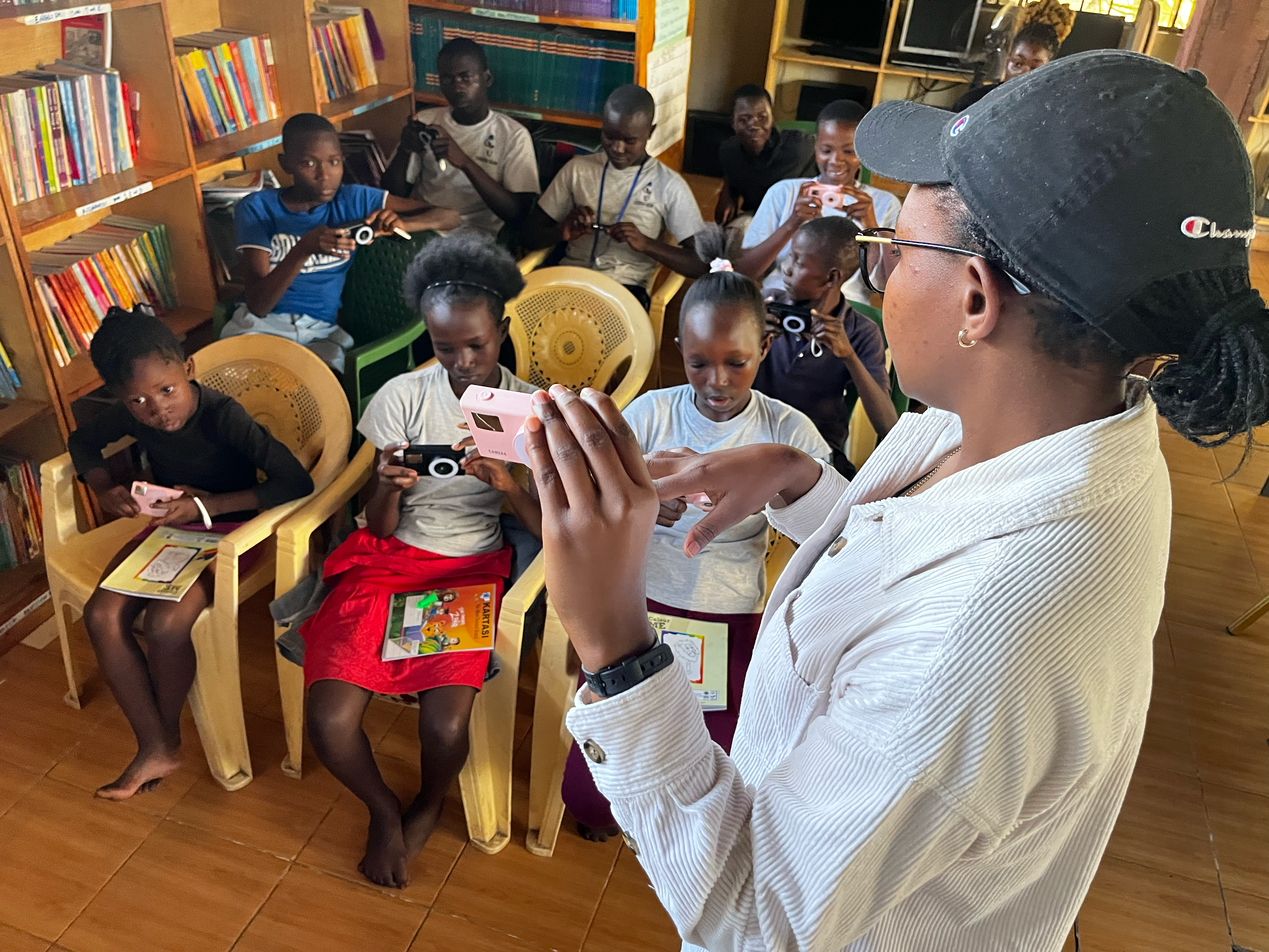 A teacher teaching a group of kids how to use a camera while in a library