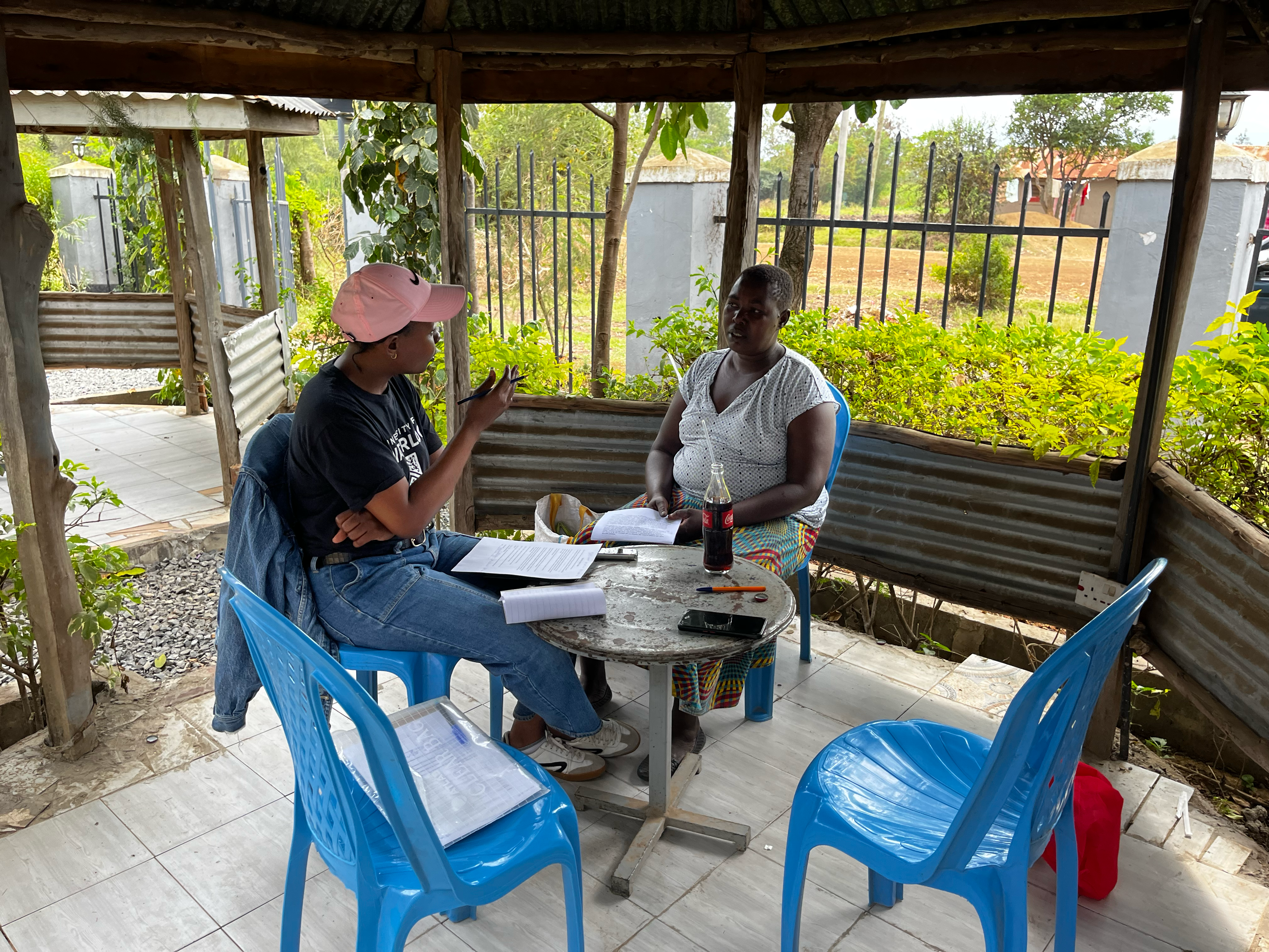 Two people sitting at a table underneath an outdoor gazebo, conducting an interview