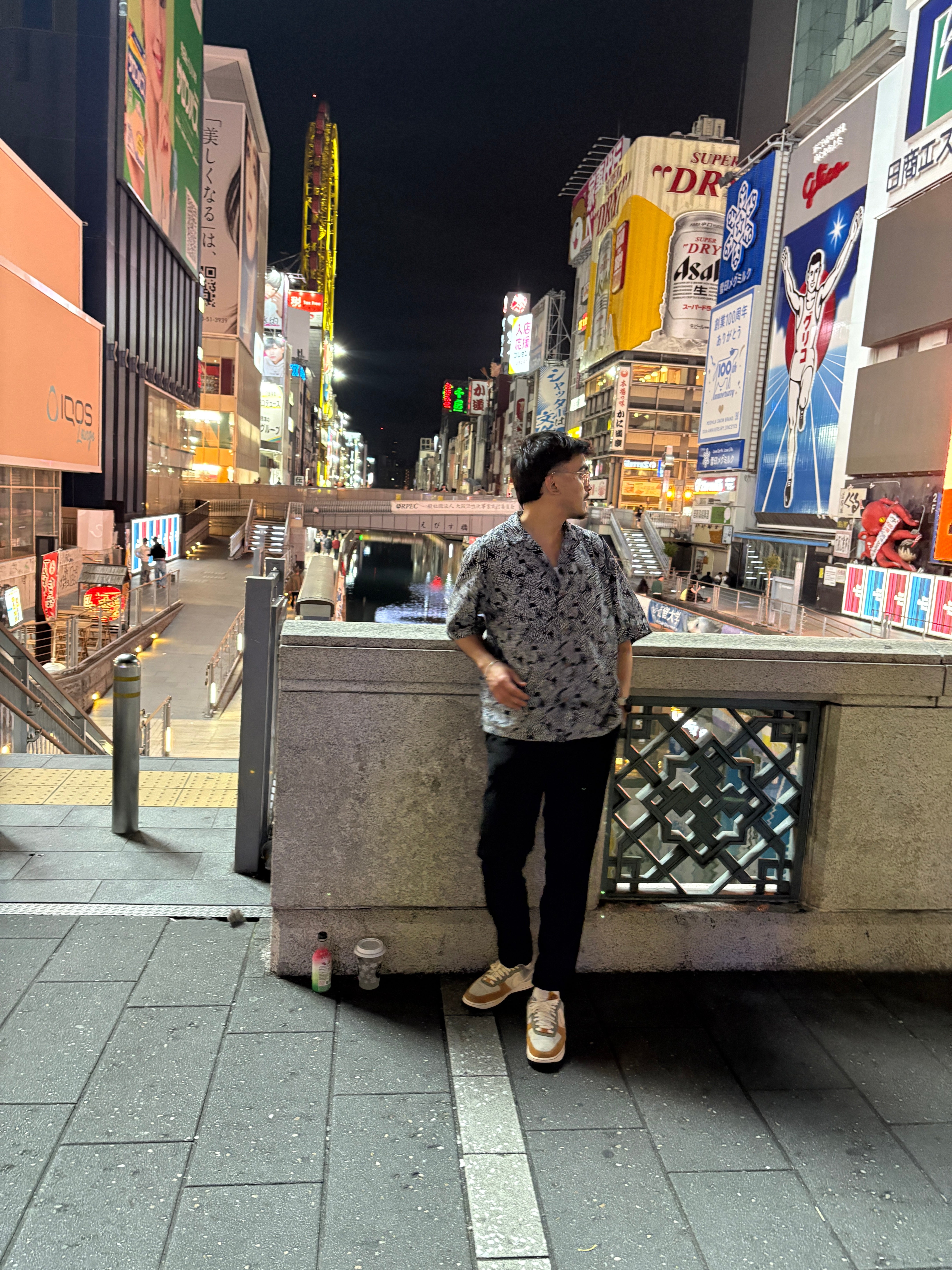 Rishabh Bajaj standing on a bridge over a river surrounded by tall buildings with advertisements on them.