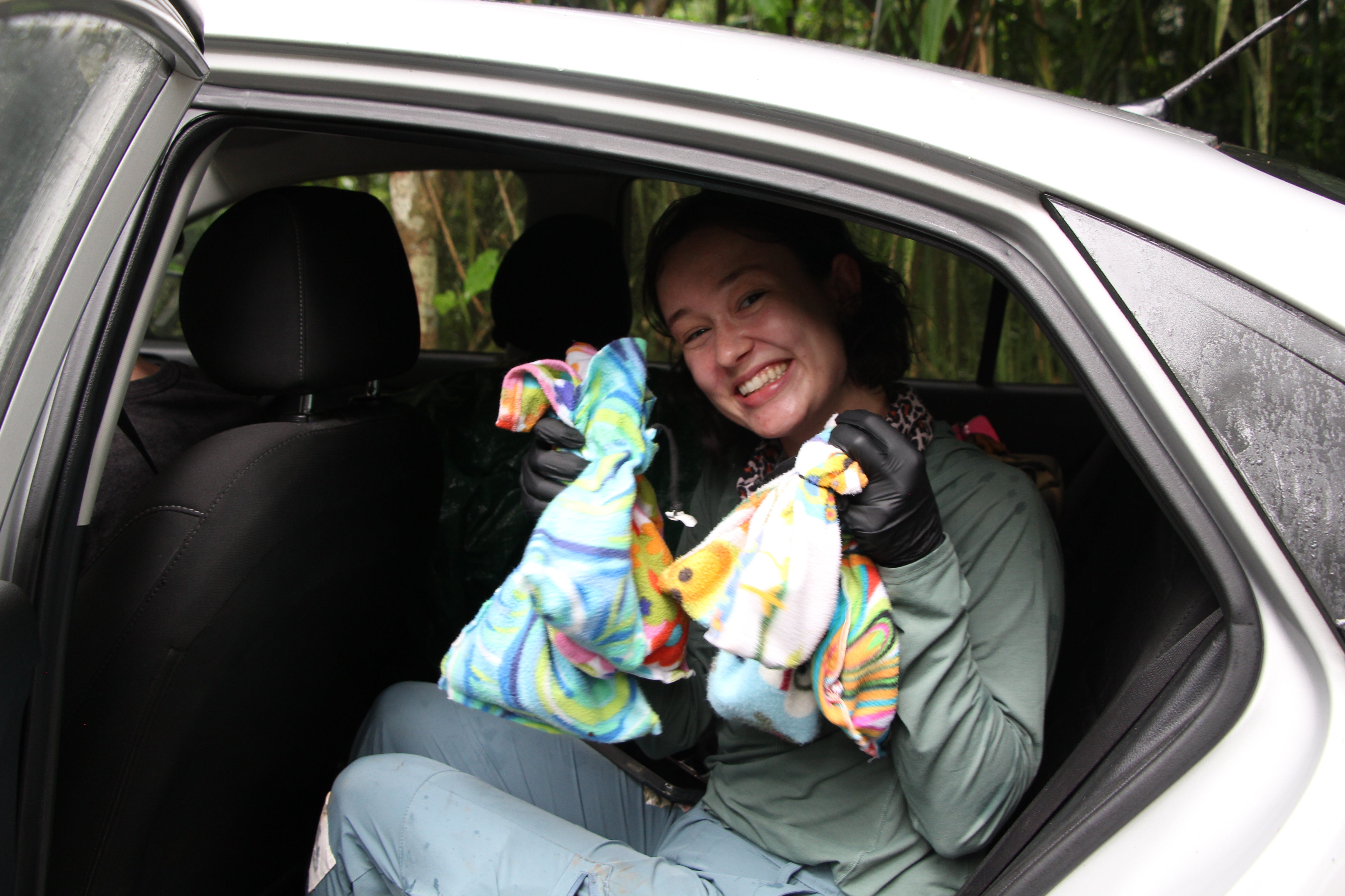 A person smiling in the back of a car holding up some bundles of cloth