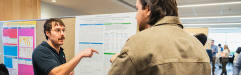 Two gentlemen speaking to each other in front of a research poster.