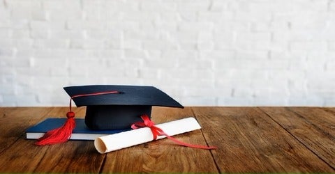 mortar board on top of book and beside scroll. grey background
