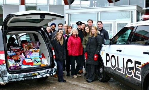 Toy drive volunteers pose with a van full of presents and a UW Police car.