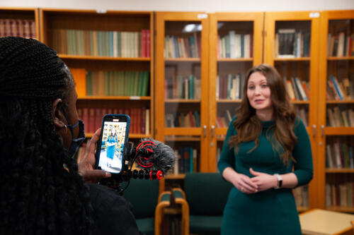 Dr. Ashley Rose Mehlenbacher speaks to a member of the media holding a camera.