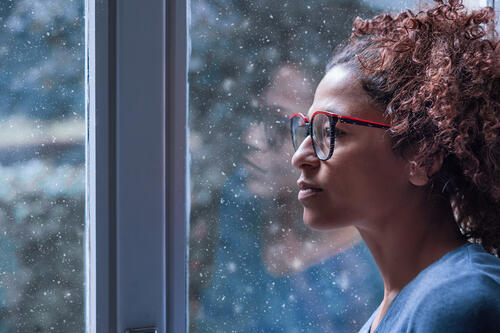 A woman looks out the window as it snows outside.