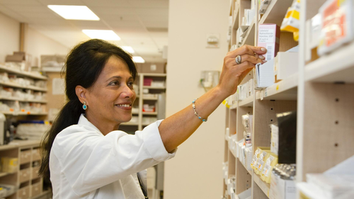 A pharmacist reaches for medicine on a shelf.