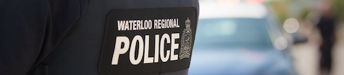 A close-up of a Waterloo Regional Police ID patch with a cruiser in the background.