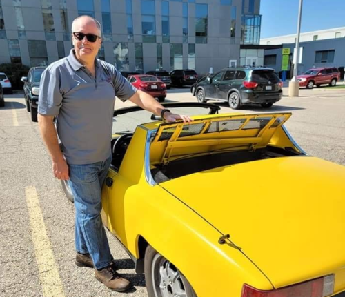 Michael Herz stands next to a yellow classic convertible sports car.