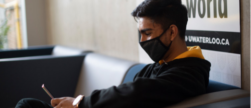 A student wearing a mask checks his smartphone.