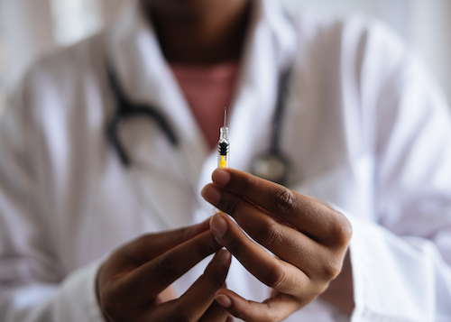 A man in a doctor's lab coat holds a needle.
