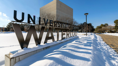 The University of Waterloo sign in winter with the Dana Porter Library in the background.