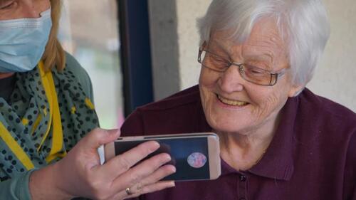 A support worker helps an LTC resident use a smart phone.