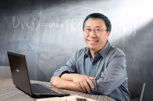Professor Ming Li sits in front of a laptop.