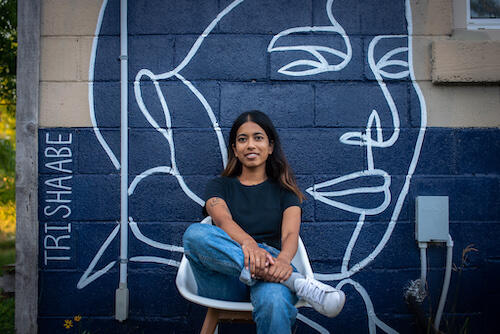 Waterloo alumnus and artist Trisha Abe sits in front of a mural.