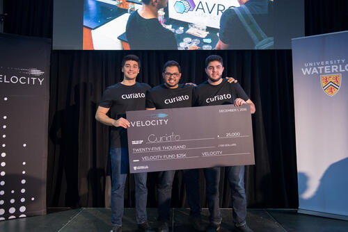 The three founders of Curiato on the Velocity Fund stage with their oversized cheque.