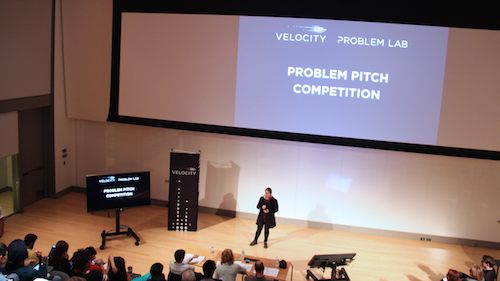 A person delivers a problem pitch on stage in the Quantum-Nano Centre.
