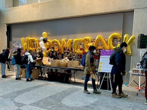 Students in mask at a welcome booth with &quot;Welcome Back&quot; spelled out in balloons.