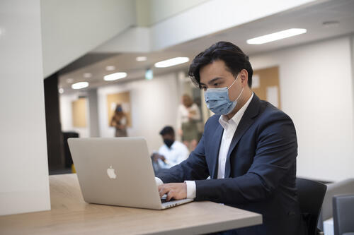 A man wearing a mask uses a laptop.