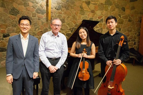 Three musicians, the finalists, stand with their instruments next to the concert sponsor.