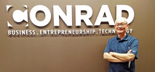 Wayne Chang stands in front of the Conrad Centre logo.