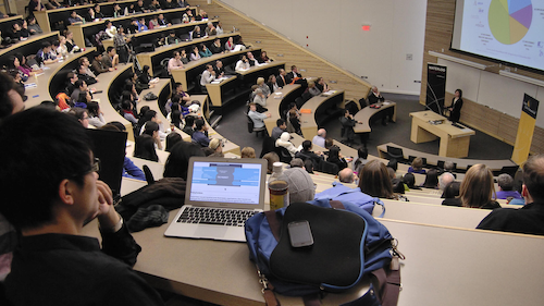 A professor delivers a lecture in a lecture hall in front of a student audience.