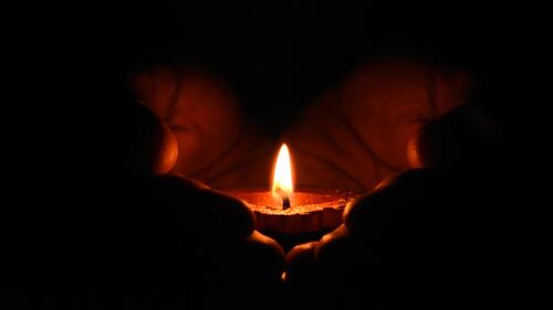 A lit candle cupped in a person's hands.