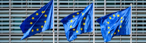 Three European Union flags flapping on poles.