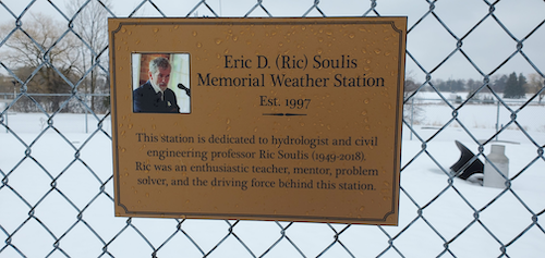 A plaque mounted on the fence surrounding the weather station noting Professor Ric Soulis.